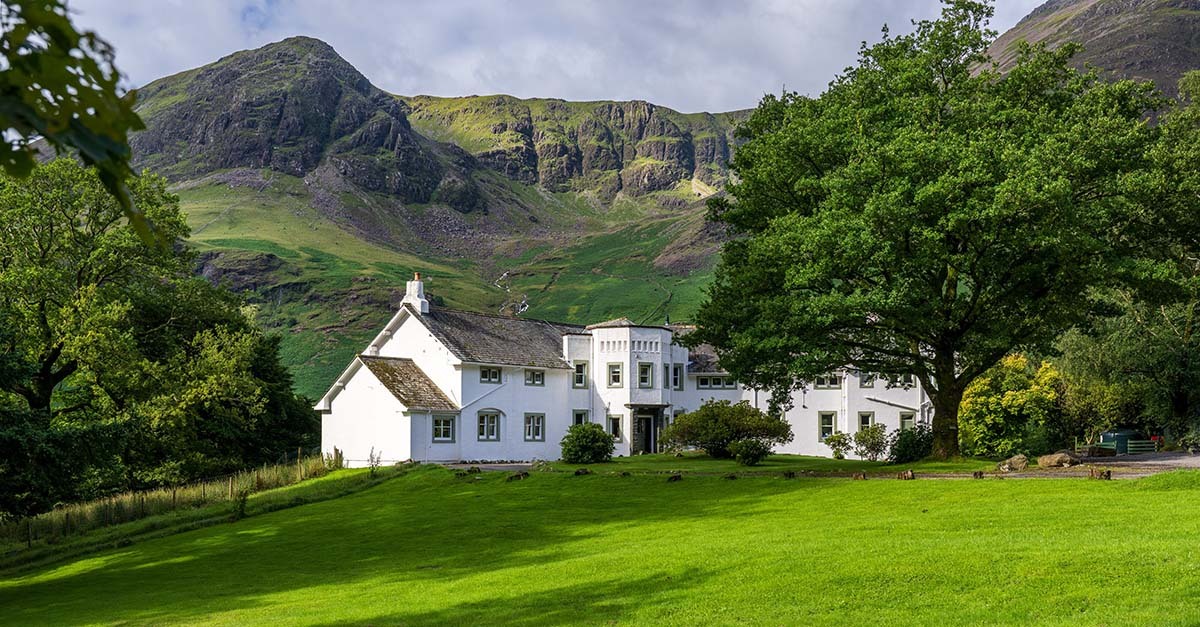 Hassness House and front garden with grass field and oak trees Robinson Fell behind